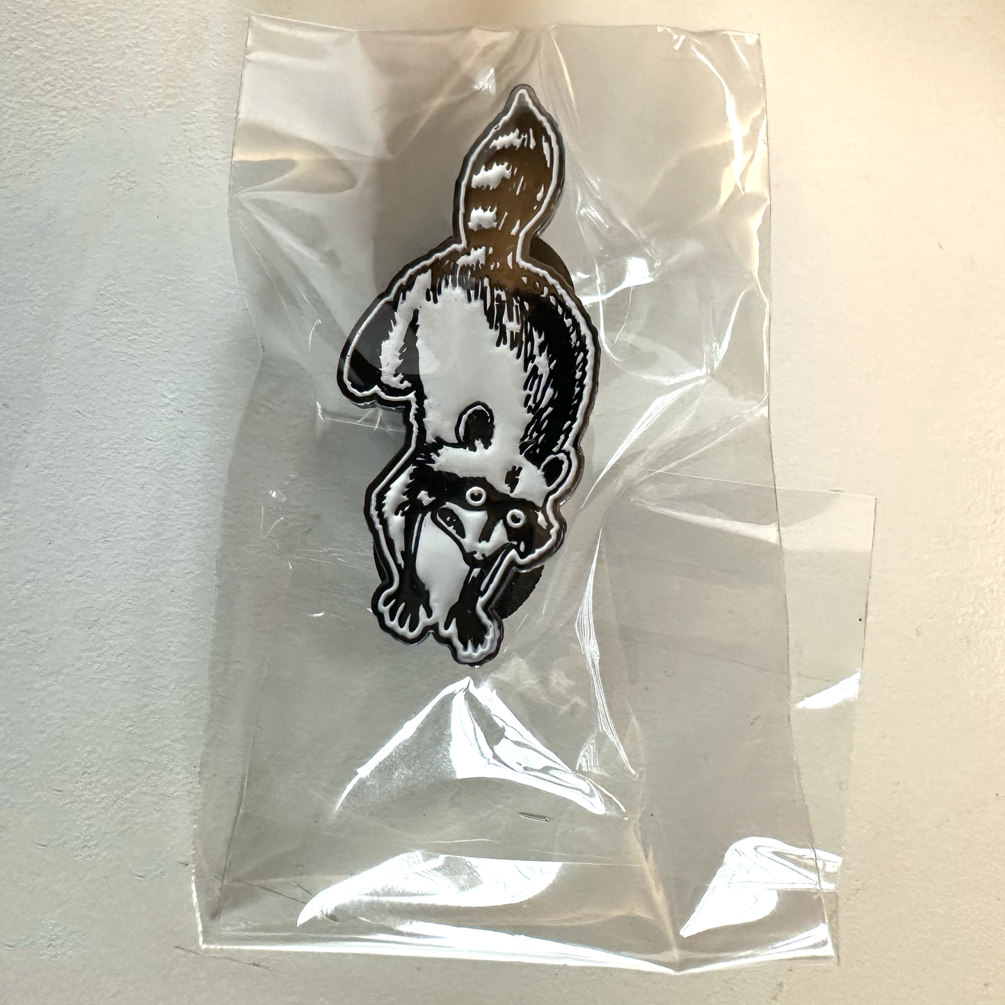 soft enamel pin of a panicking raccoon in a plastic bag