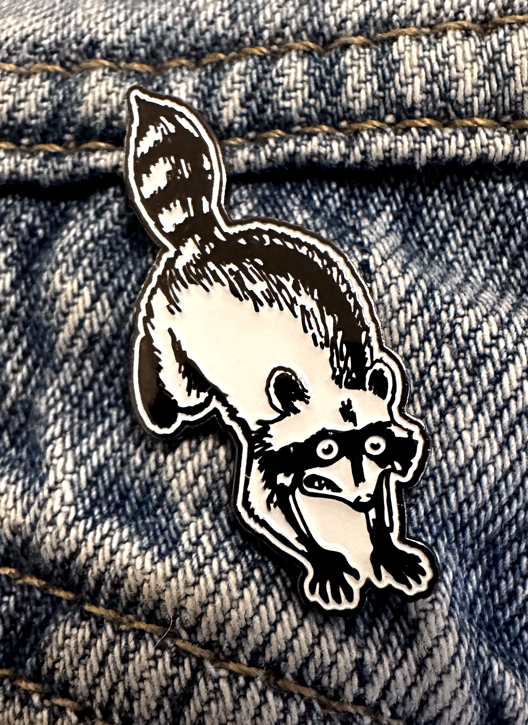 soft enamel pin of a panicking raccoon on a denim jacket